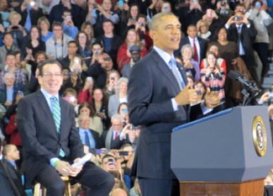Gov. Dannel P. Malloy sits behind President Obama during a rally in New Britain promoting the President's push to increase the minimum wage in 2014