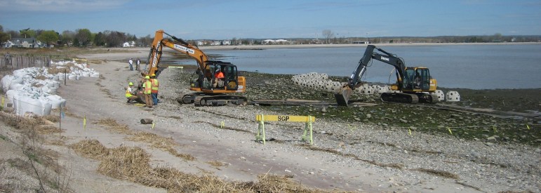 Behind the Reef Balls, there are damaged dunes with geotube exposure and sandbags.