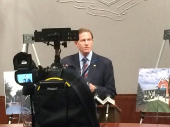 U.S. Sen. Richard Blumenthal standing with pictures of Clinton Crossing.
