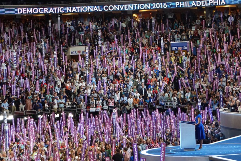 Michelle Obama at the podium among a sea of purple "Michelle" signs.