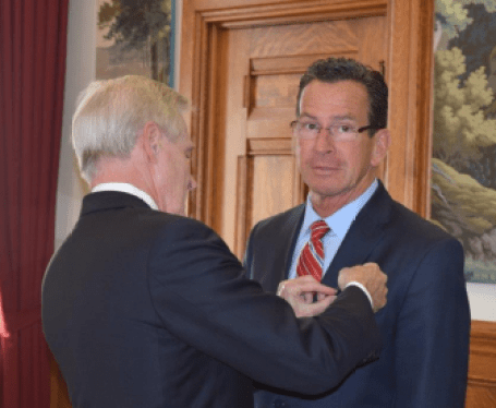 Navy Secretary Ray Mabus pinning a medal on a self-conscious Gov. Dannel P. Malloy.