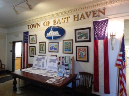 An art display in East Haven Town Hall between two American flag banners.