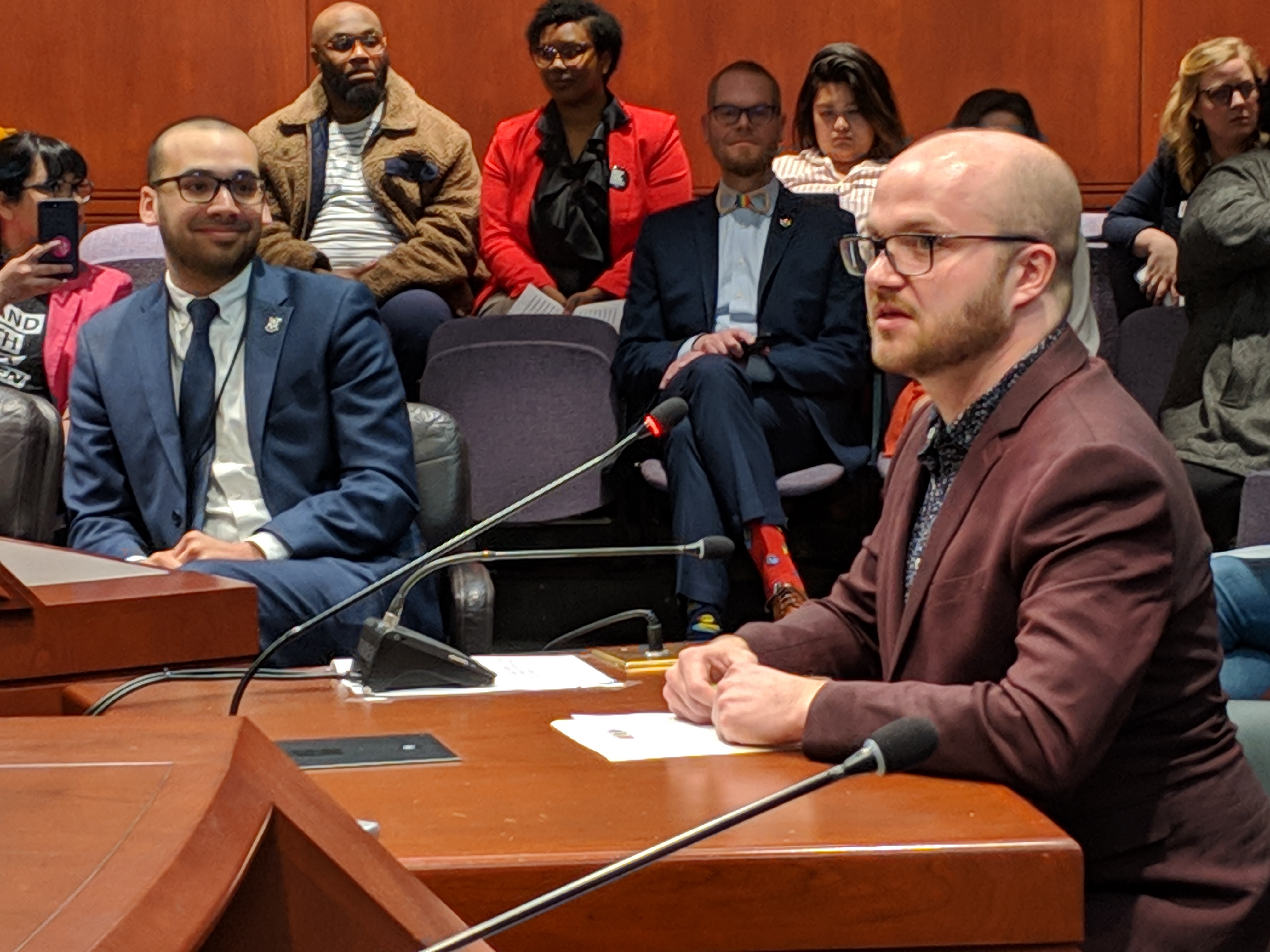 Conor Pfeifer, a development officer with Triangle Community Center. voices support for a bill to establish a Lesbian, Gay, Bisexual, Transgender and Queer Health and Human Services Network. Rep. Raghib Allie-Brennan, at left, co-proposed the bill.