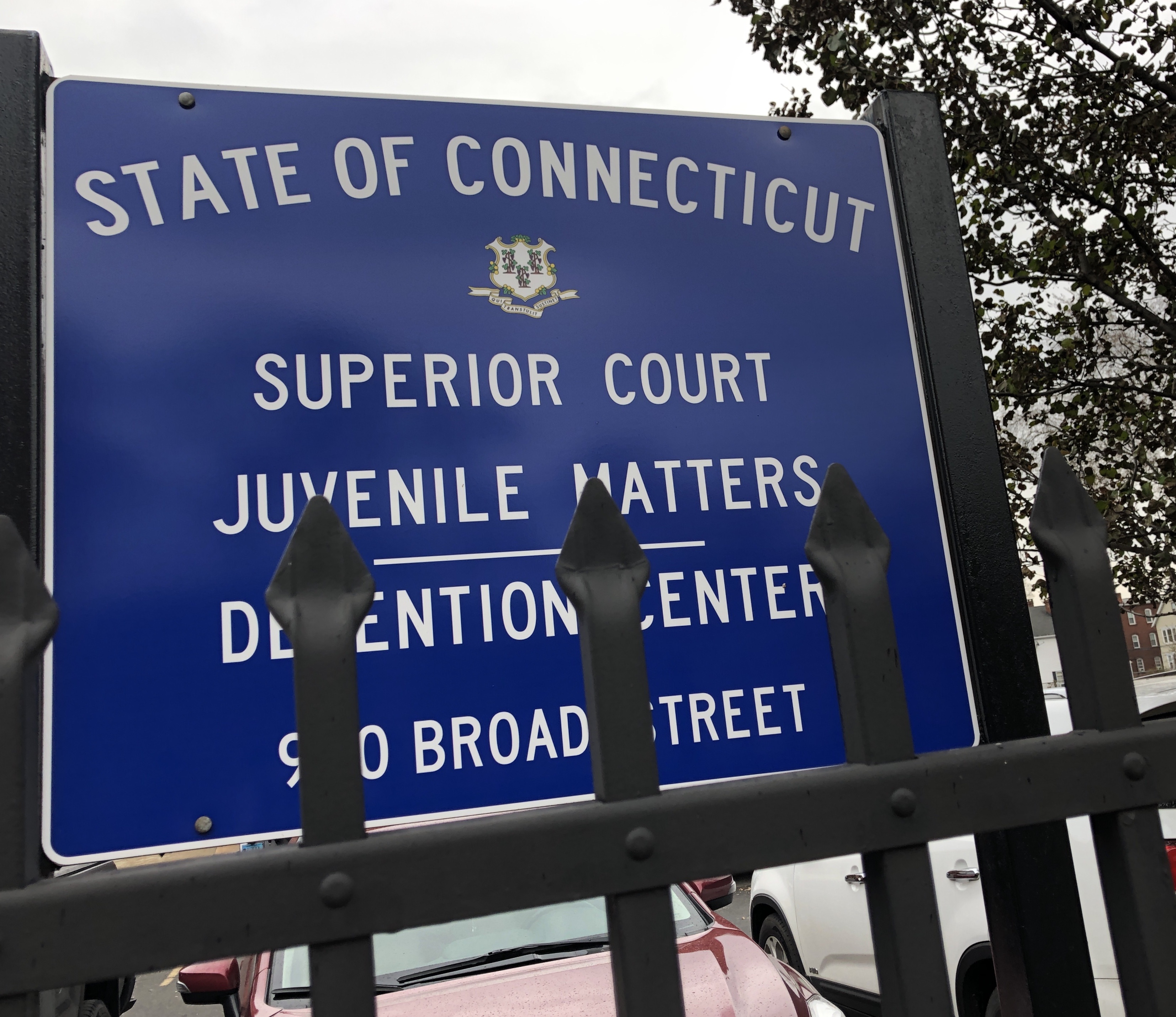 A photo of a blue sign in front of the Hartford Juvenile Detention Center. A gate is seen in front of the sign.