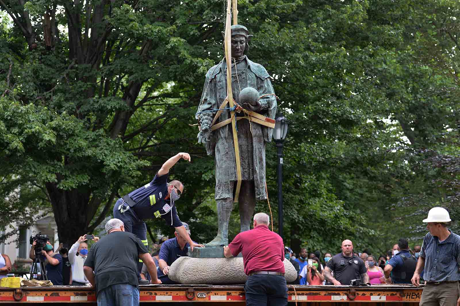 Construction workers move a statue of Christopher Columbus with rope tied around it