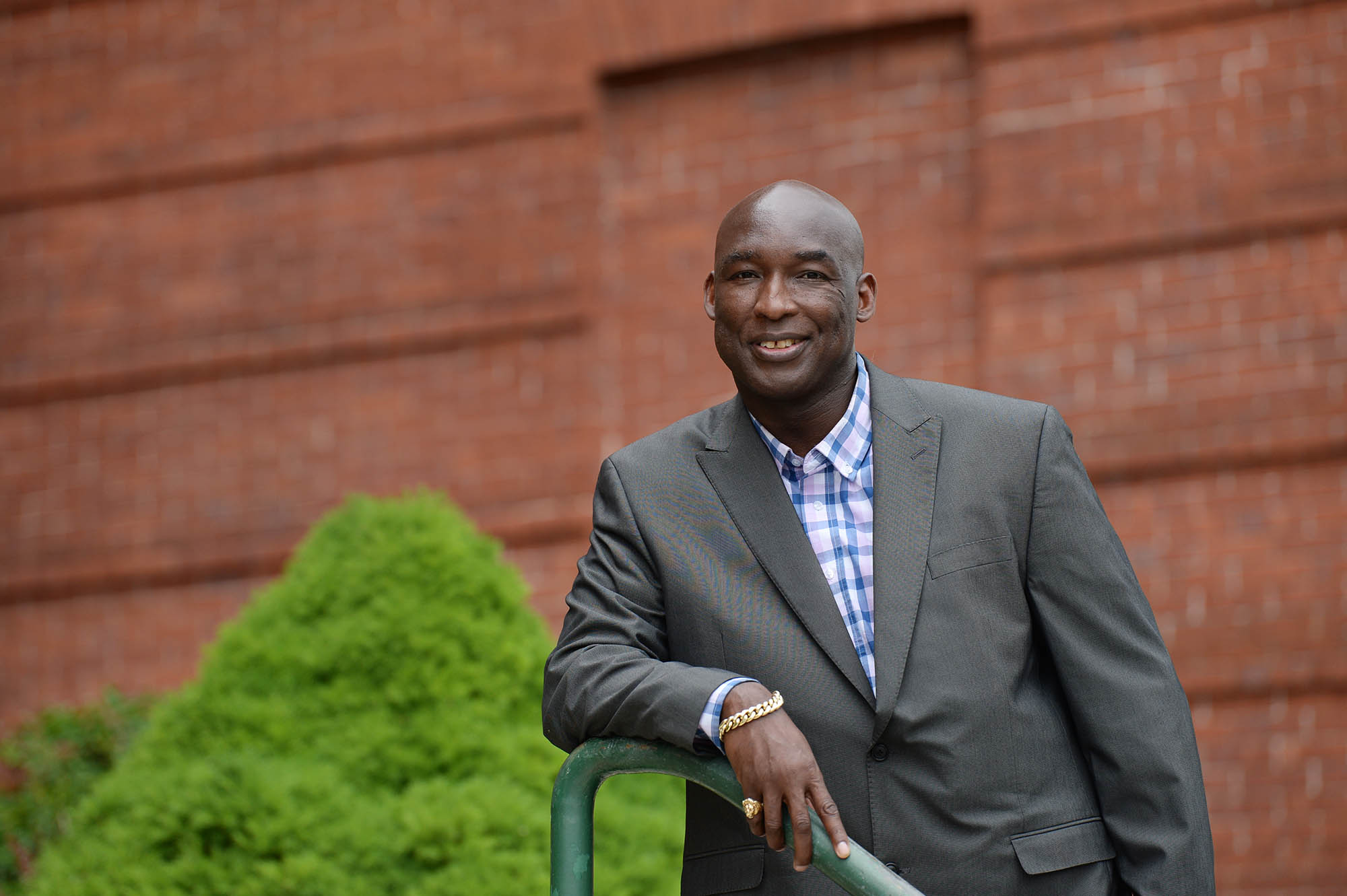 Daryl McGraw, wearing a suit jacket and a pink and blue button up shirt, leans on a rail and smiles for a portrait photo.