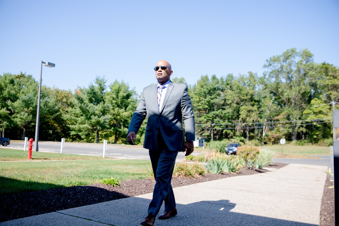 Angel Quiros, Connecticut's Department of Correction commissioner, makes his way up a sidewalk, wearing a gray suit and sunglasses.