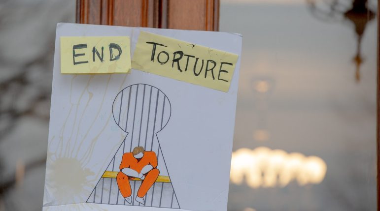 A sign that says "End Torture," with an illustration of a prisoner sitting in a cell alone.