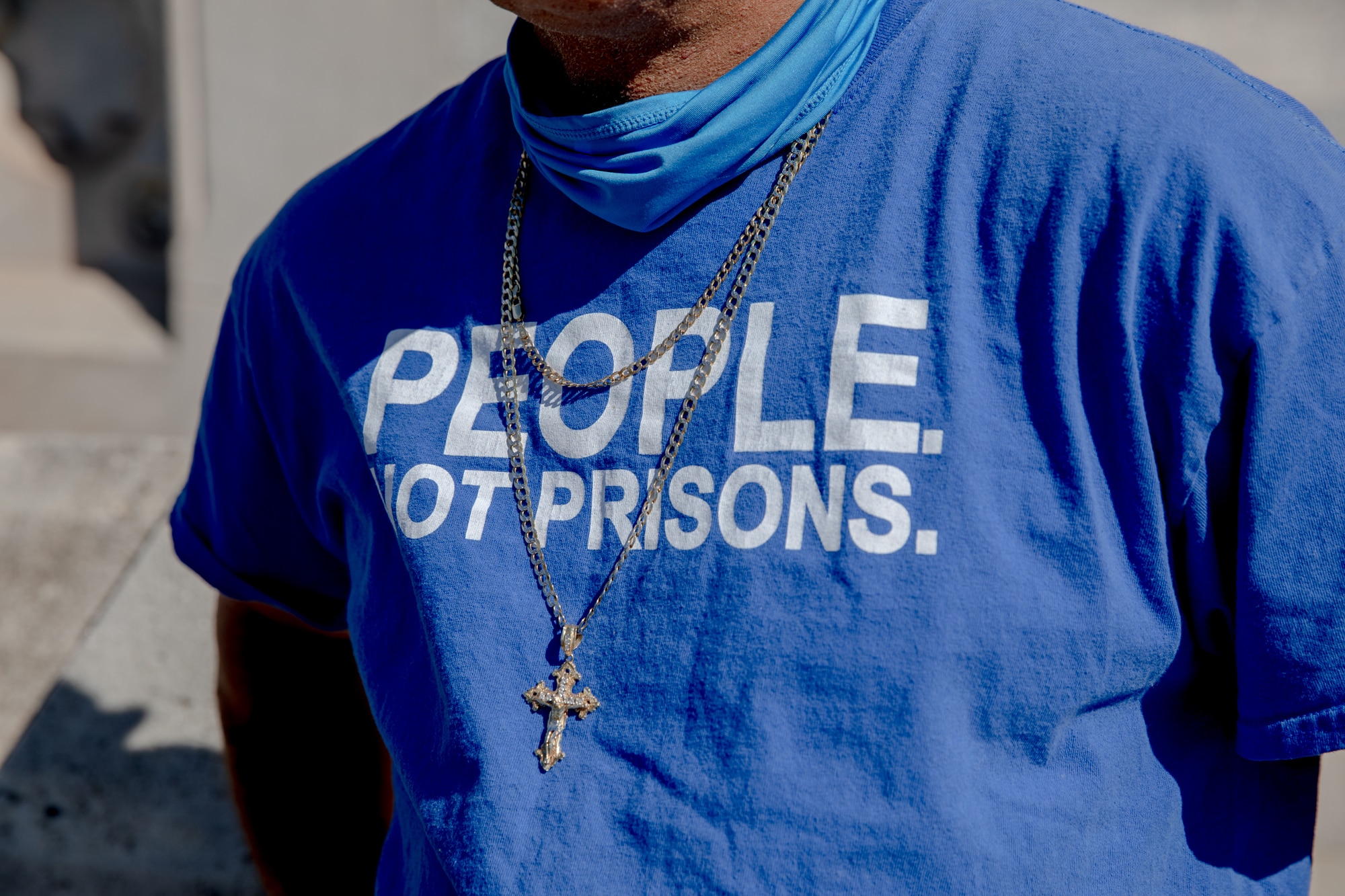 A person wearing a cross and a blue shirt with the phrase, 'People Not Prisons."