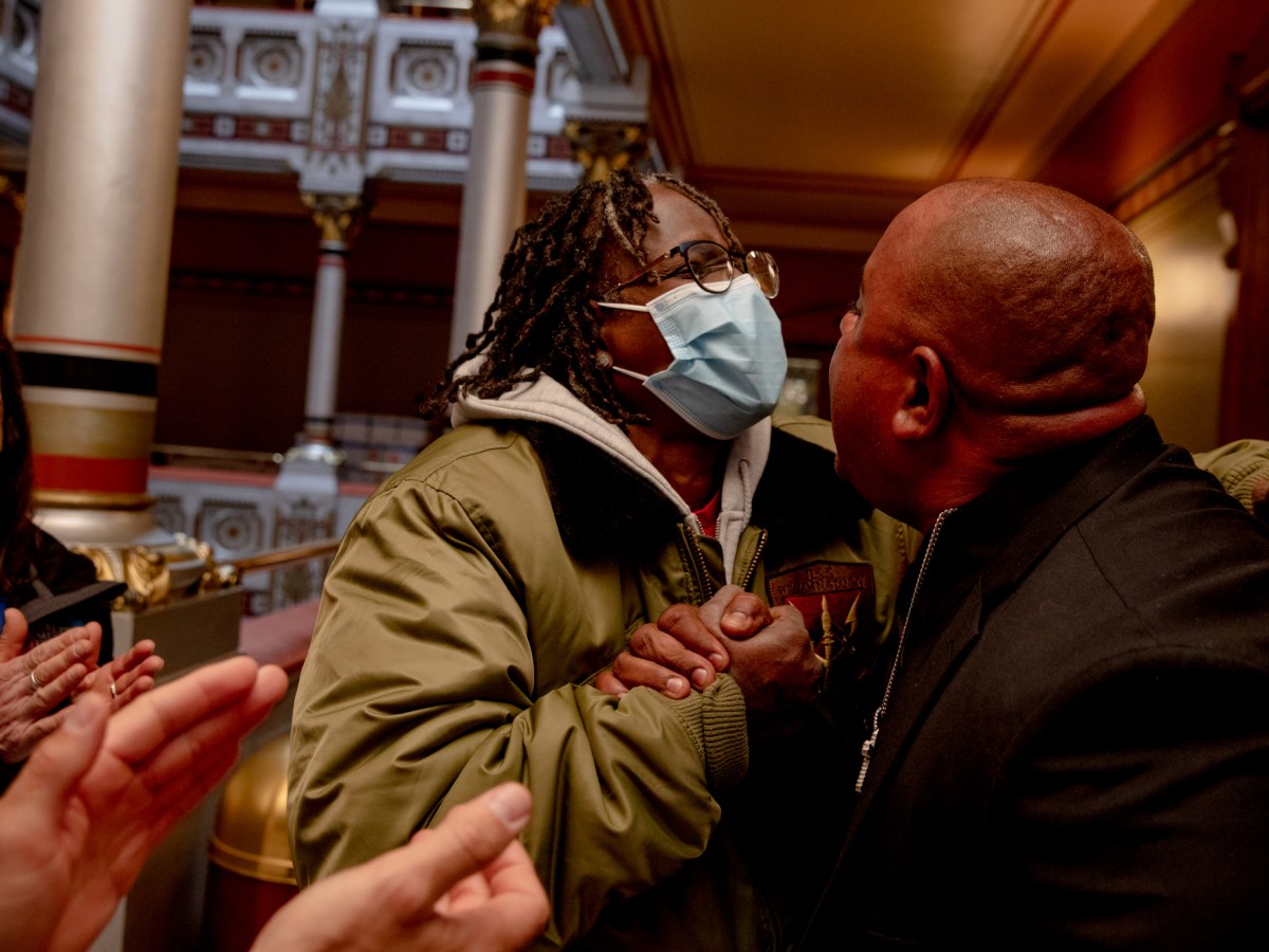 Terri Ricks, an advocate for the ACLU of Connecticut, embraces Virgilio Rosario, the brother of a Connecticut state representative, embrace each other in a hallway of the Connecticut State Capitol Building. They are gripping hands. Both look emotional and joyful.
