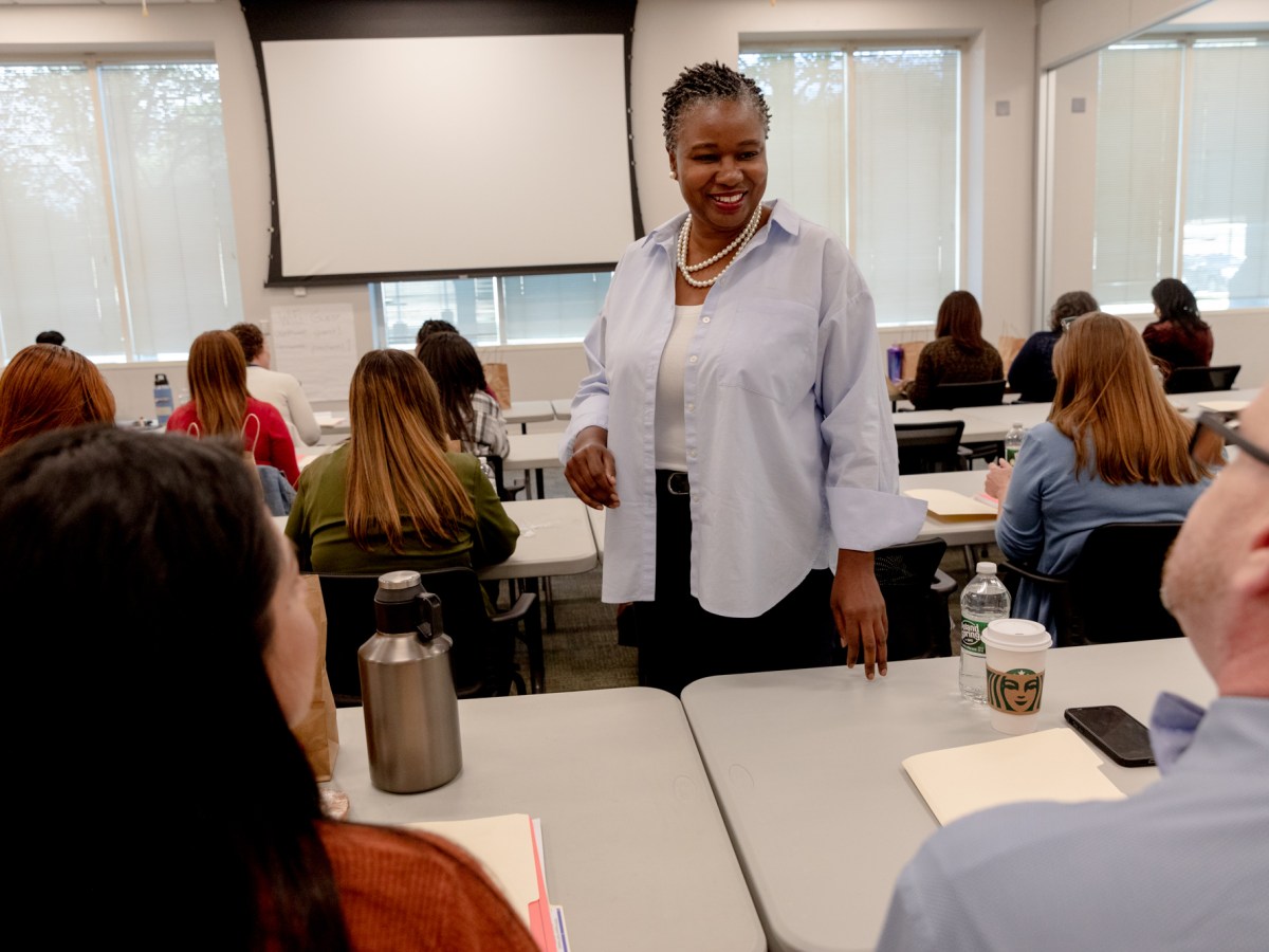 TaShun Bowden-Lewis, Connecticut's chief public defender, stands and smiles while greeting two of her colleagues who are sitting down.