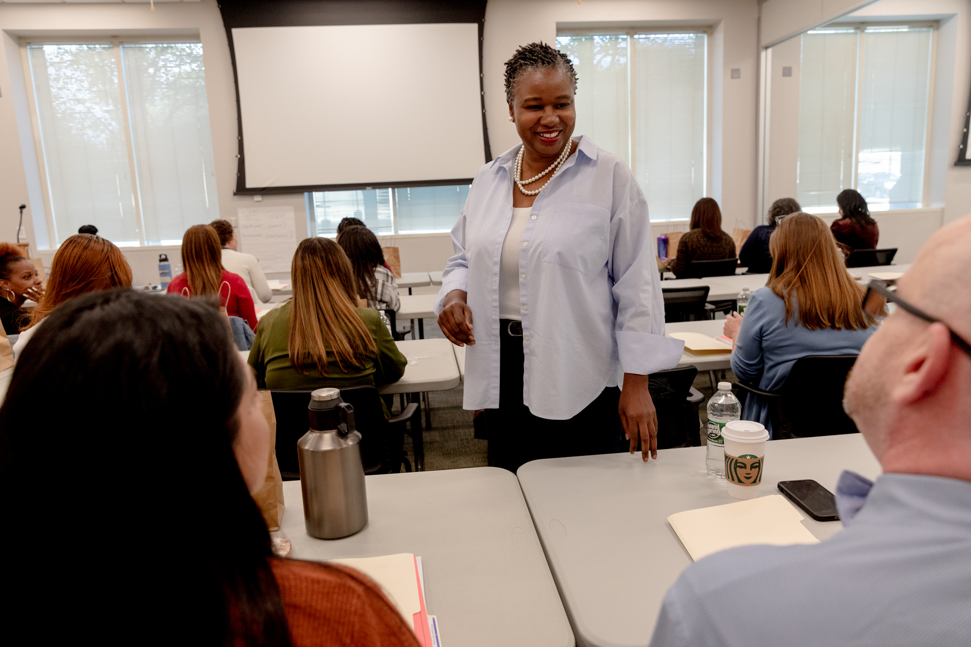TaShun Bowden-Lewis, Connecticut's chief public defender, stands and smiles while greeting two of her colleagues who are sitting down.