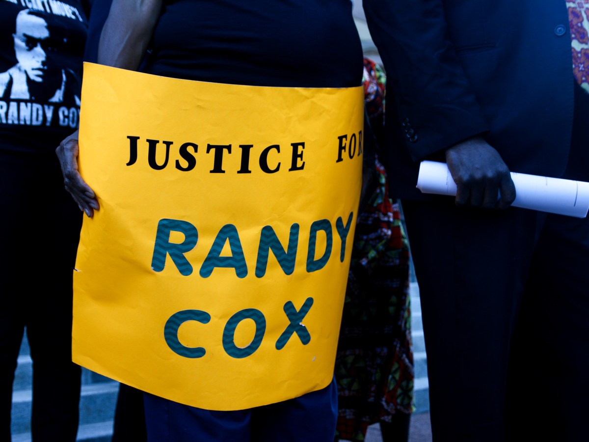 A family member of Randy Cox holds a gold poster that reads, "Justice for Randy Cox."