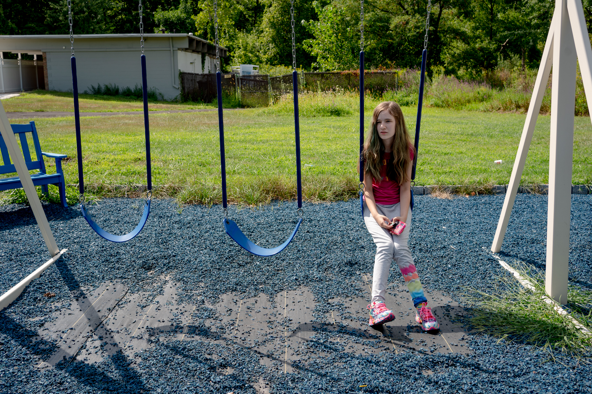 A girl sits alone on a swing set. It's a sunny day and grass is behind her.
