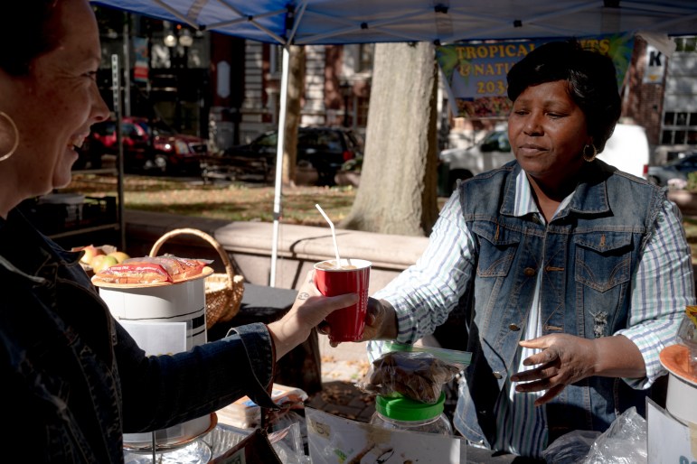 Una mujer que trabaja en un mercado de granjeros le da jugo de tamarindo a un cliente sonriente.