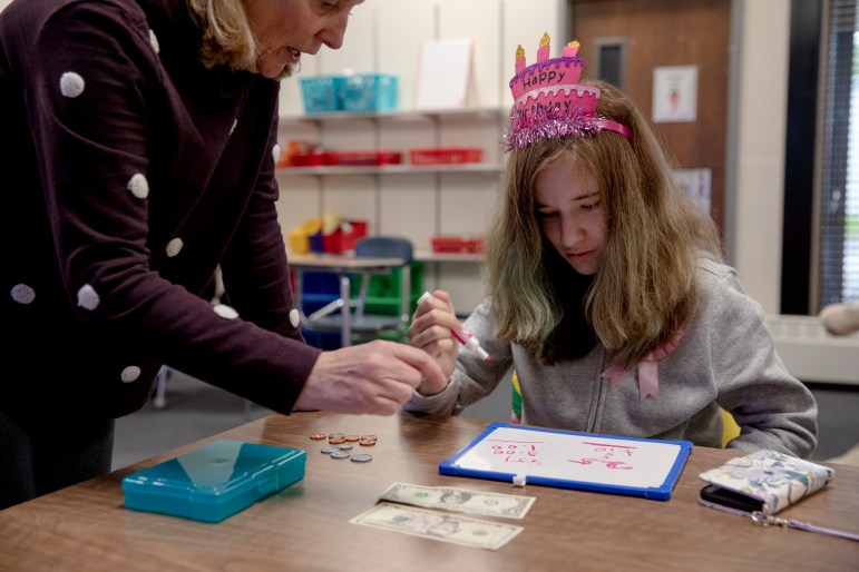 A girl writes on a dry erase board with a pink marker. She is learning to do the math required to make purchases.