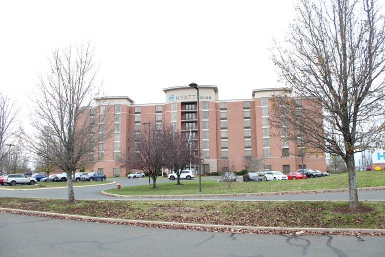 A tall building, the Hyatt House Hotel, is seen standing in between two trees without leaves.