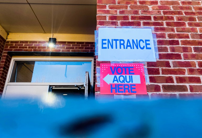 An entry way to an election day polling location, with two signs that say "Entrance" and "Vote Aqui Here," respectively.