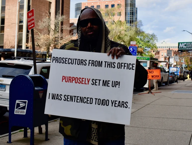 Darcus Henry holds a sign that reads "Prosecutors from this office purposely set me up! I was sentenced to 100 years."
