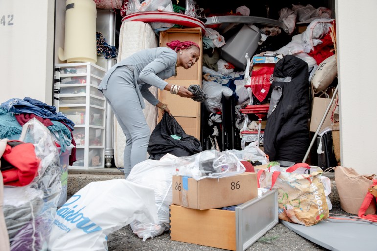 Una mujer vestida de gris saca ropa de una bolsa de basura frente a su atestada unidad de almacenamiento.