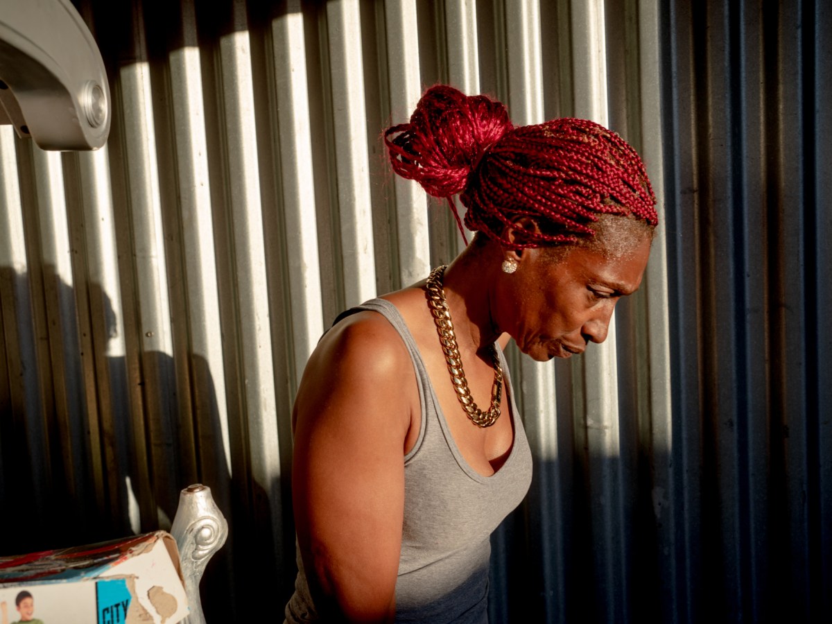 A woman in a grey tank top stands, head bowed, at her storage unit.