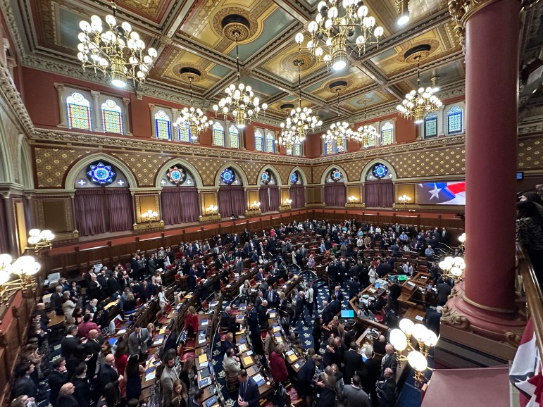 Connecticut legislators converse in the House chamber of the State Capitol building, a room with good lighting.