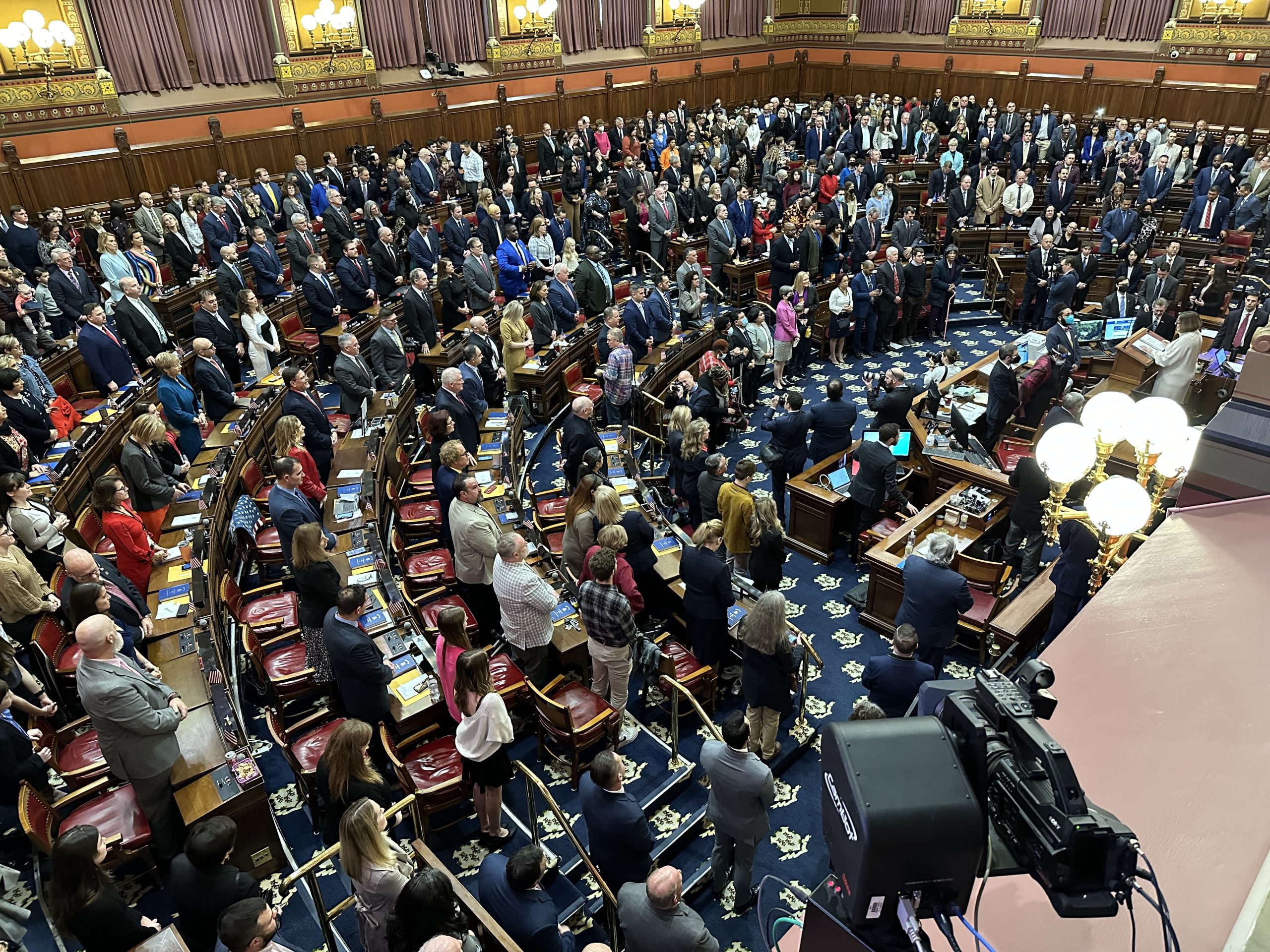 Connecticut legislators converse in the House chamber of the State Capitol building, a room with good lighting.