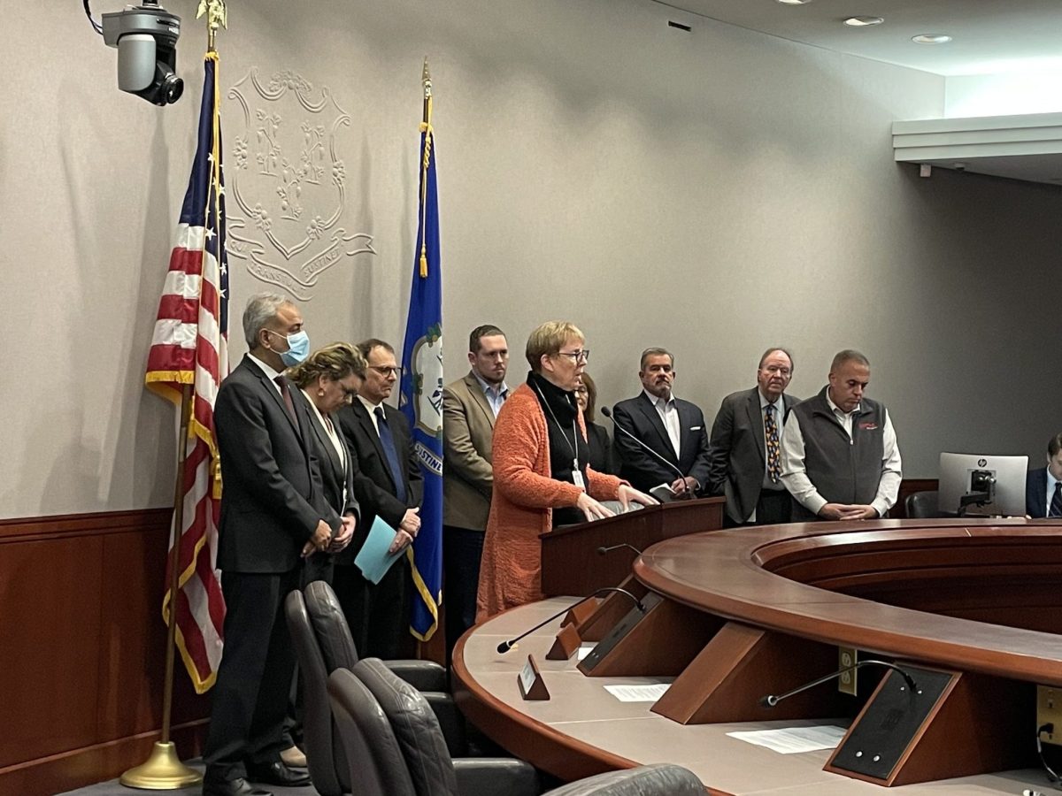 A legislator stands at a lectern with several other legislators and advocates behind her.
