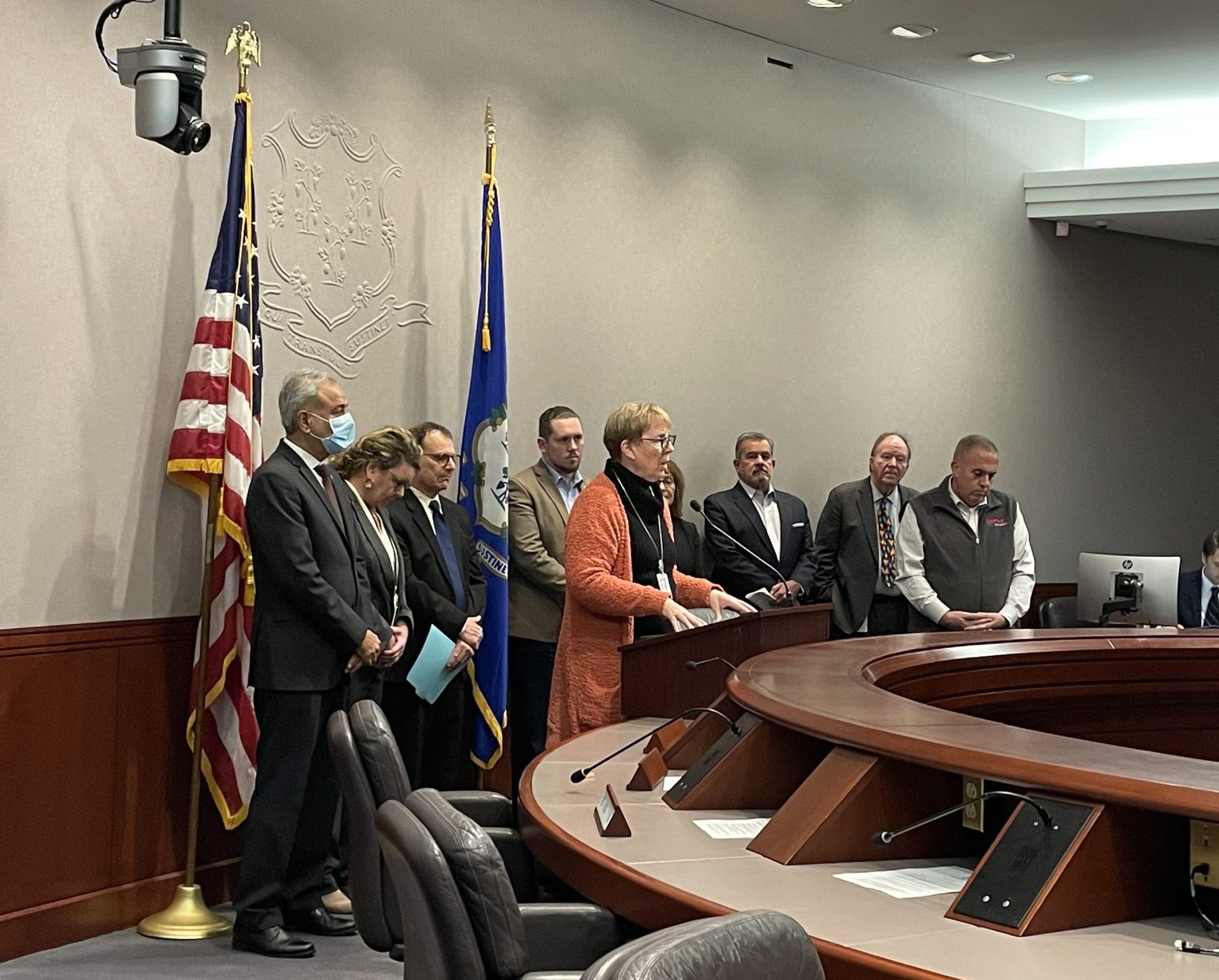 A legislator stands at a lectern with several other legislators and advocates behind her.