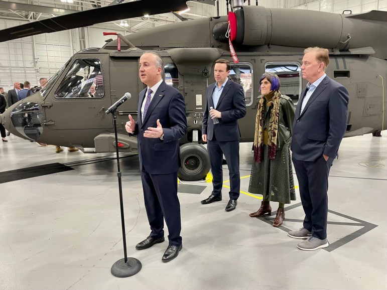 Four people stand in front of a Blackhawk helicopter inside the Sikorsky plant.