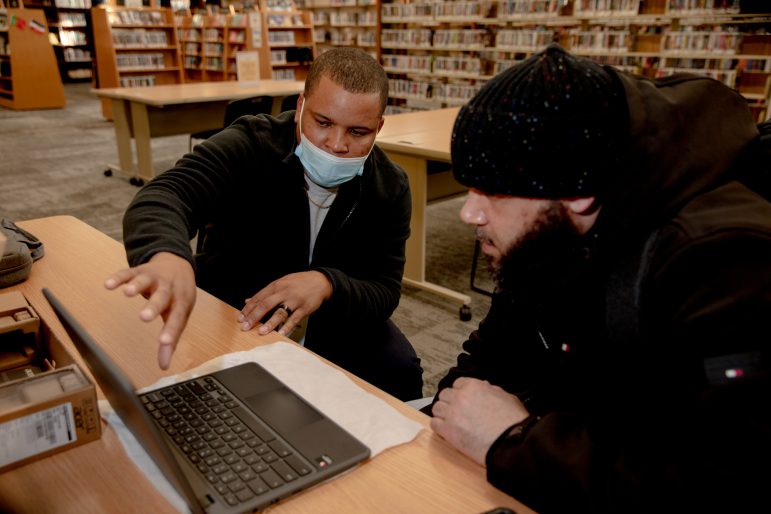 Dos hombres se sientan en un escritorio con una computadora portátil.