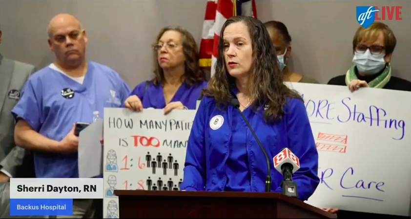 Una mujer con uniforme de enfermera azul se para en un podio hablando por un micrófono.