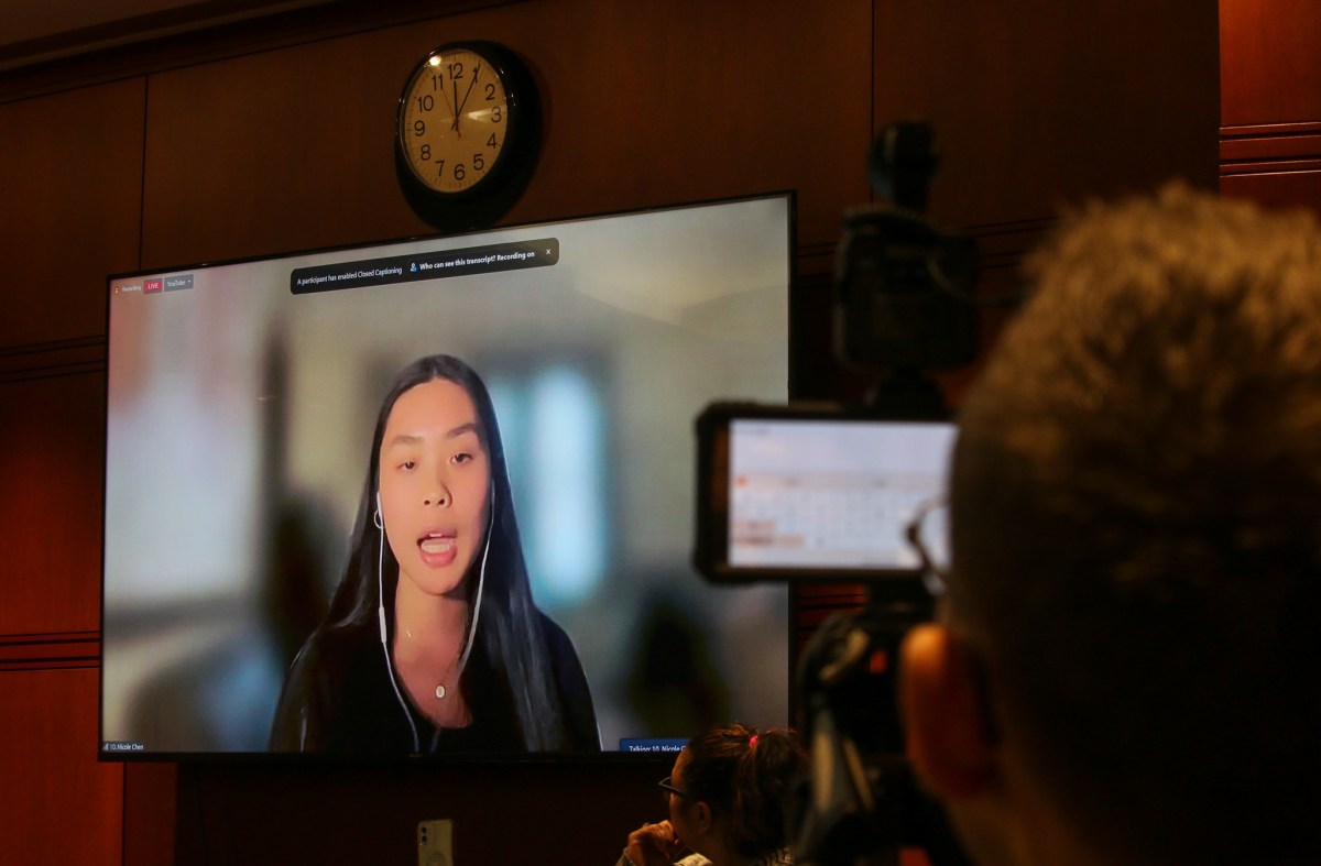 Nicole Chen, a student at Yale University, is seen through a TV, talking to legislators virtually. A clock is above the TV showing Chen, who has a blurred background and is participating through video chat.