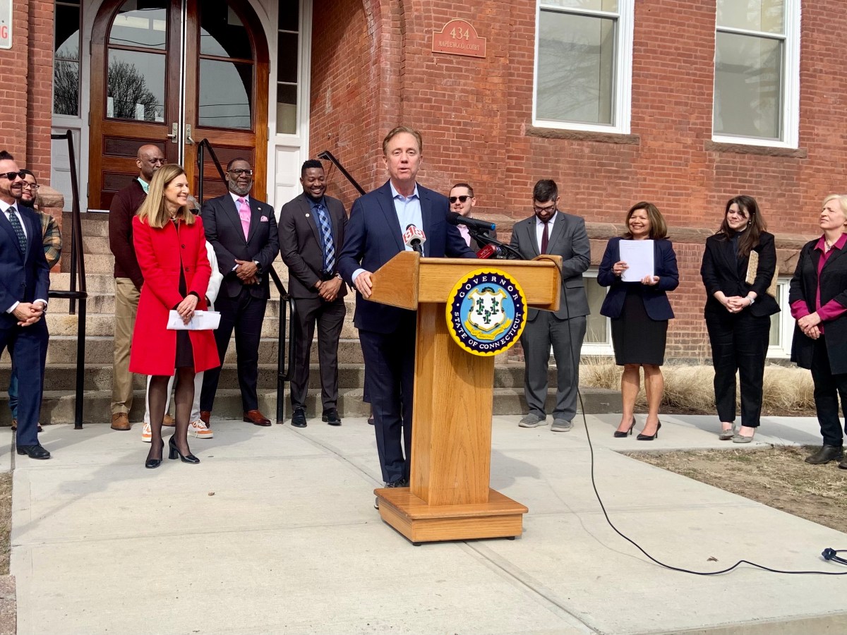 Gov. Ned Lamont stands in front of a building in Bridgeport with other officials on either side.