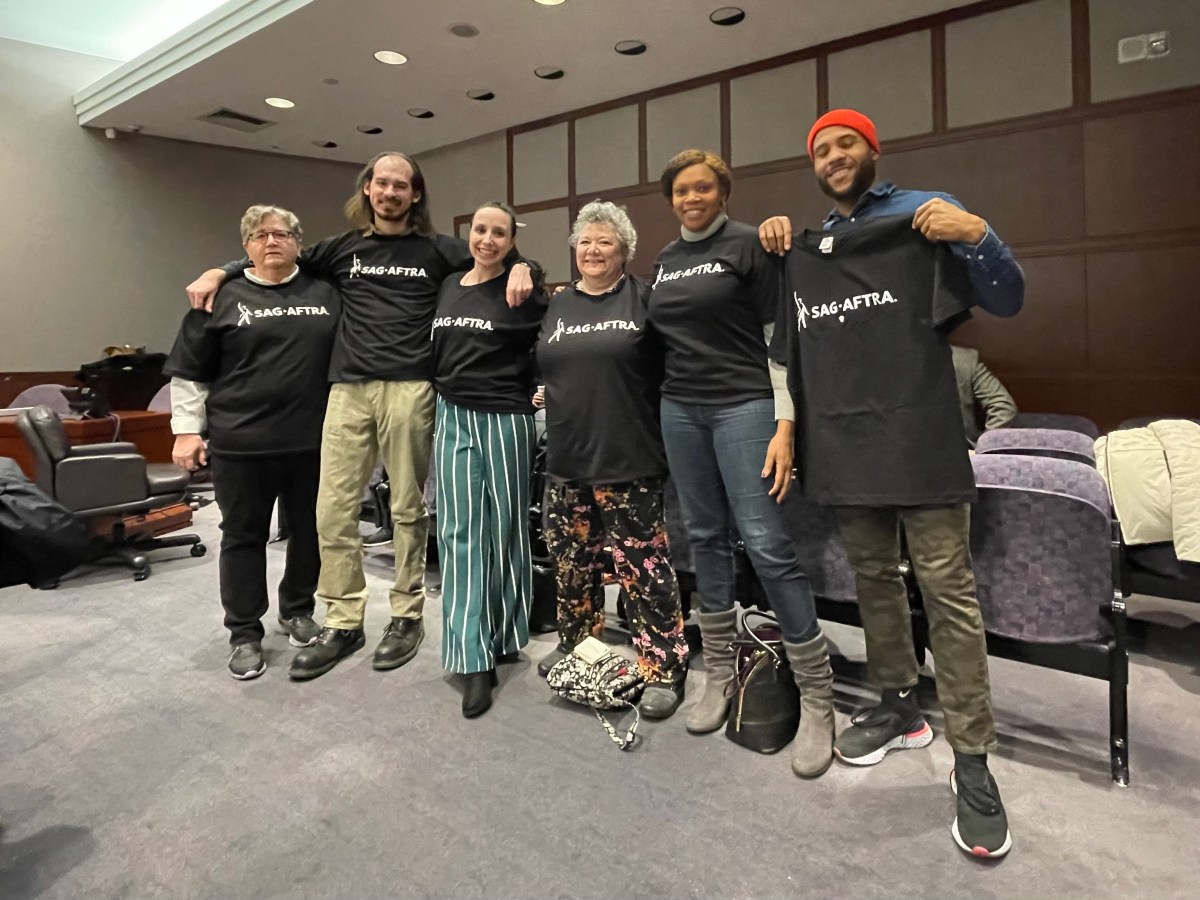 Six people in a legislative hearing room wearing t-shirts with the SAG-AFTRA logo.