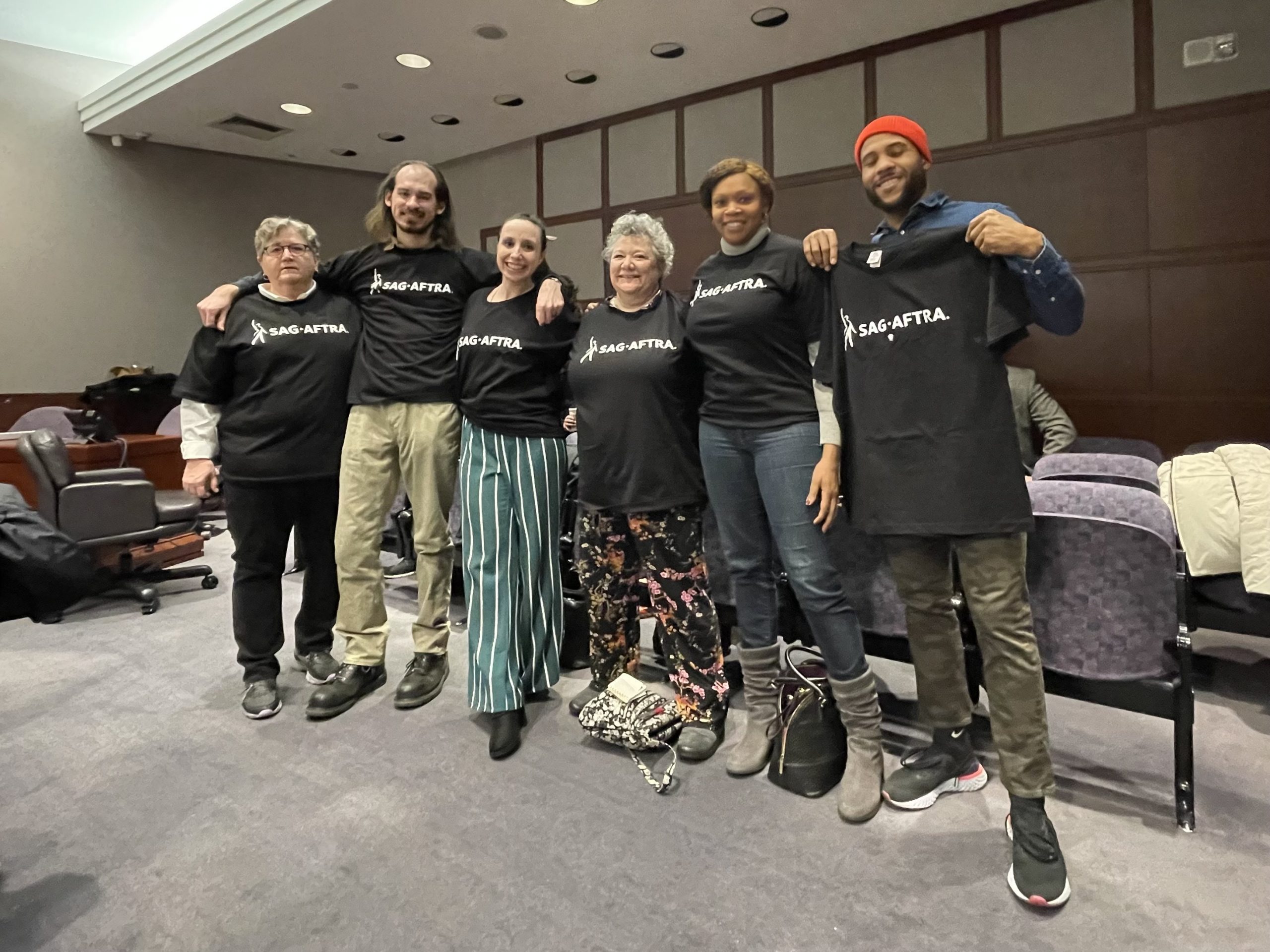 Six people in a legislative hearing room wearing t-shirts with the SAG-AFTRA logo.