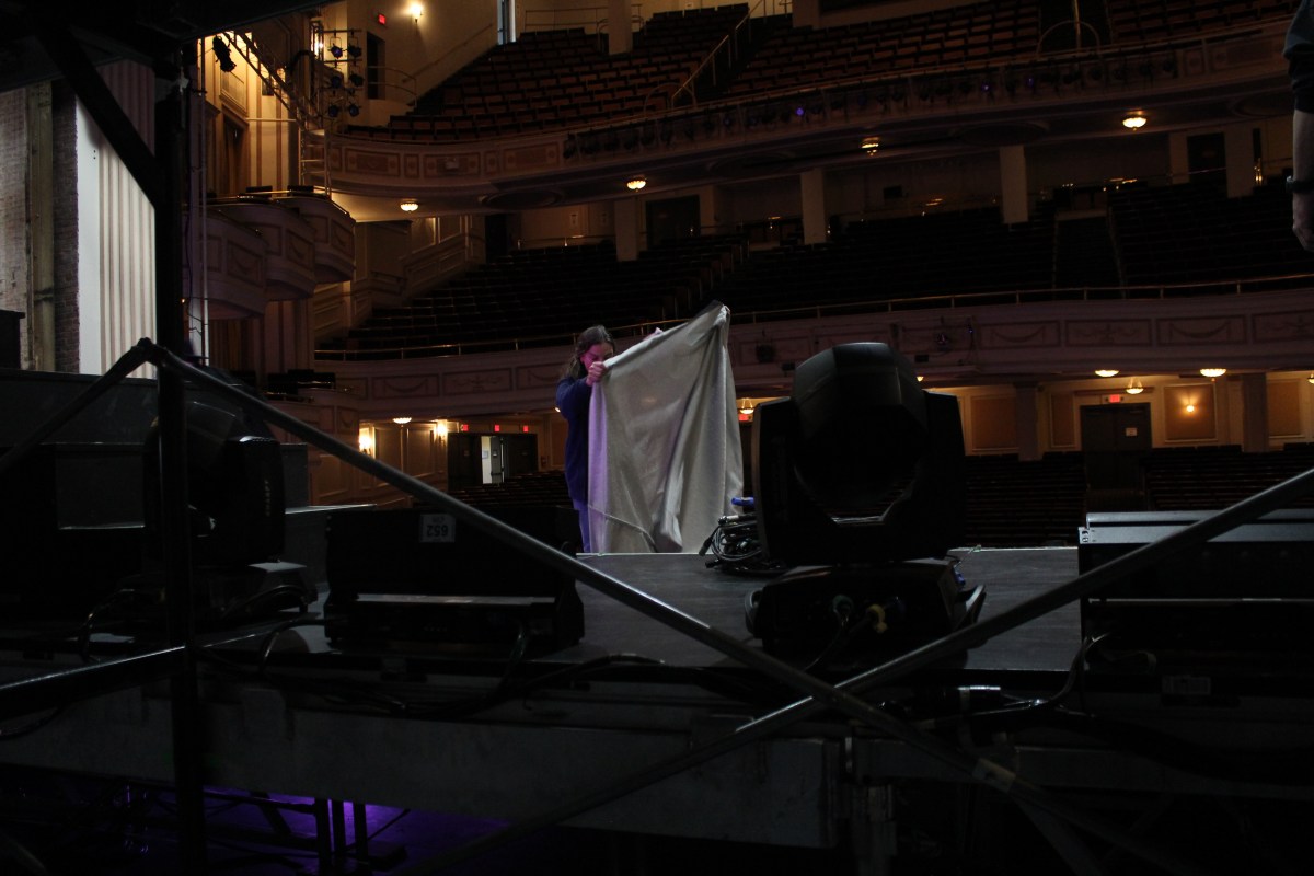 A stagehand holds up fabric on a dark stage.