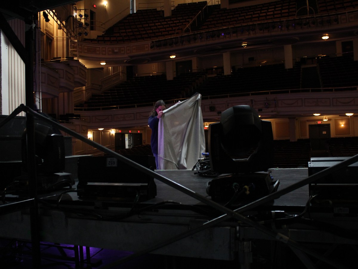 A stagehand holds up fabric on a dark stage.