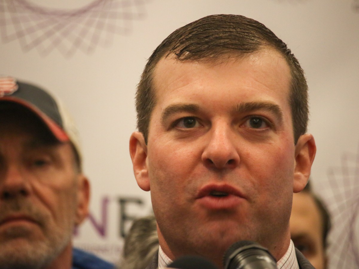Rep. Steven Stafstrom looks ahead as he speaks into a microphone. Two people are seen standing behind him.