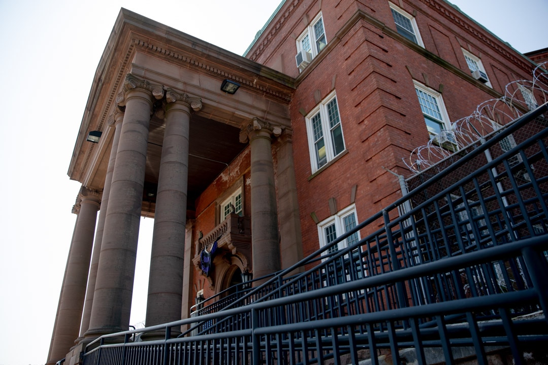 The exterior front of Cheshire Correctional Facility during the day time. The building has a red-like color and has several floors. Windows are seen from the outside.