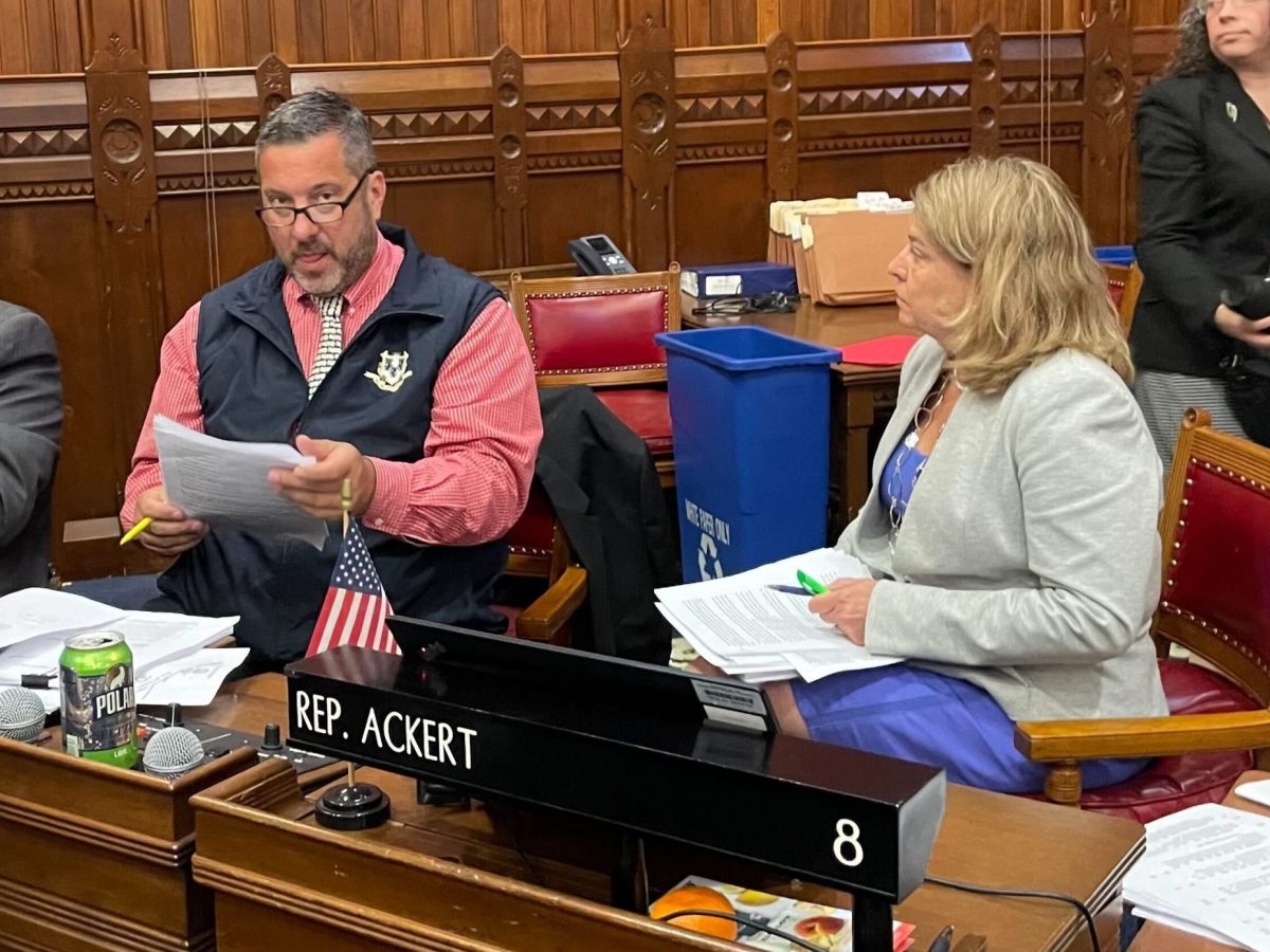 Two people sit at a desk in a wood paneled room.