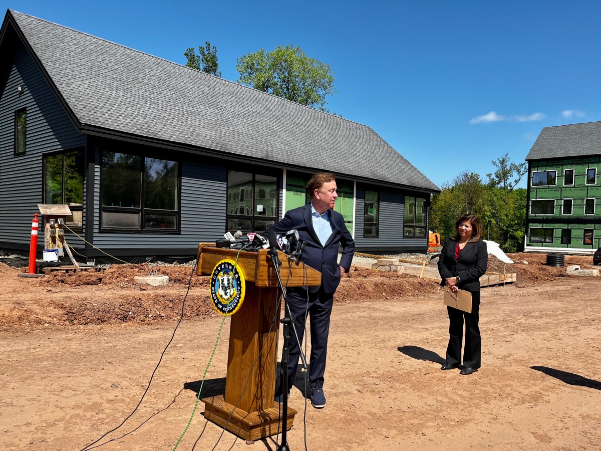 The governor stands at a podium in front of a construction site for new apartments in Newington, Connecticut.