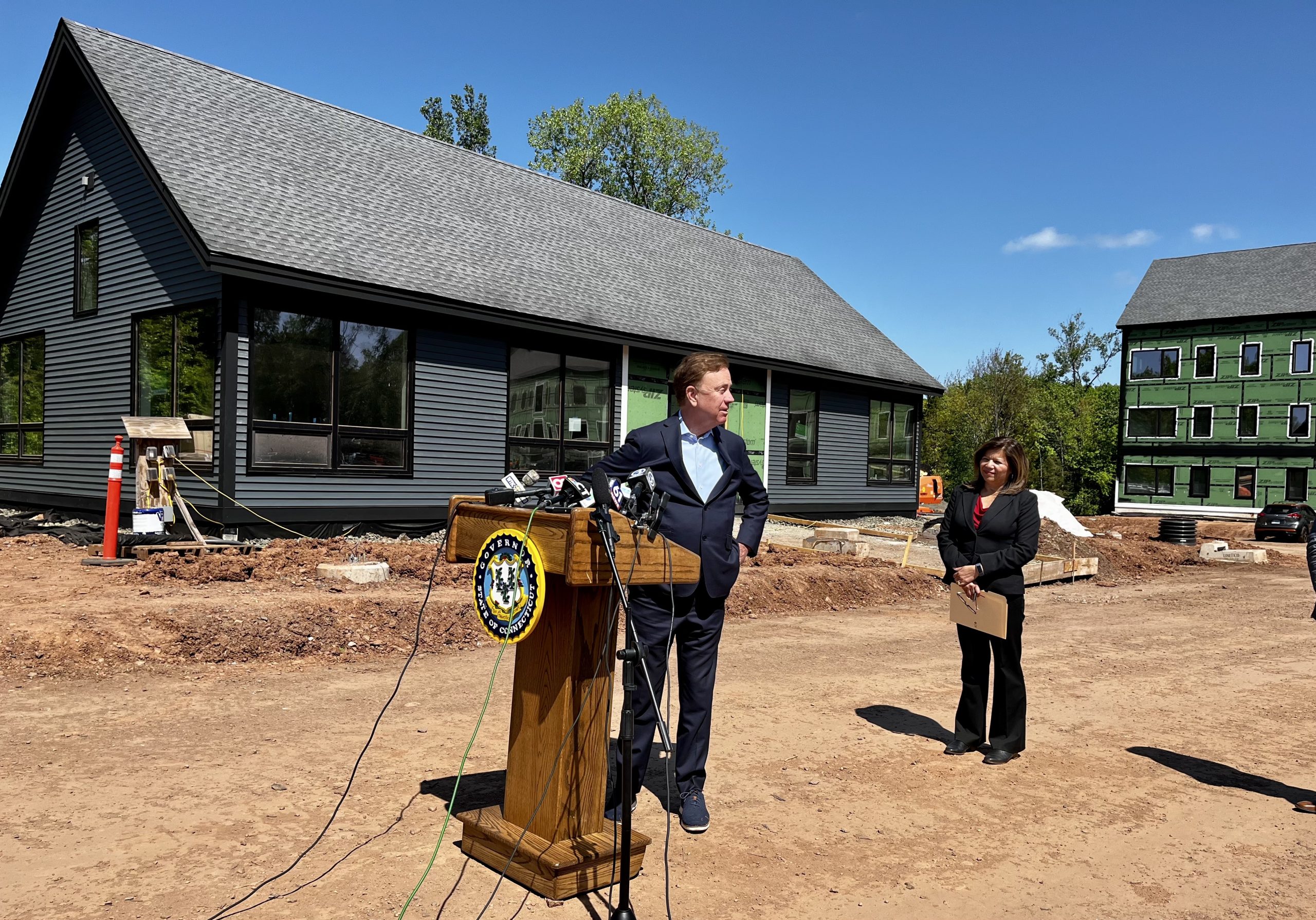 The governor stands at a podium in front of a construction site for new apartments in Newington, Connecticut.