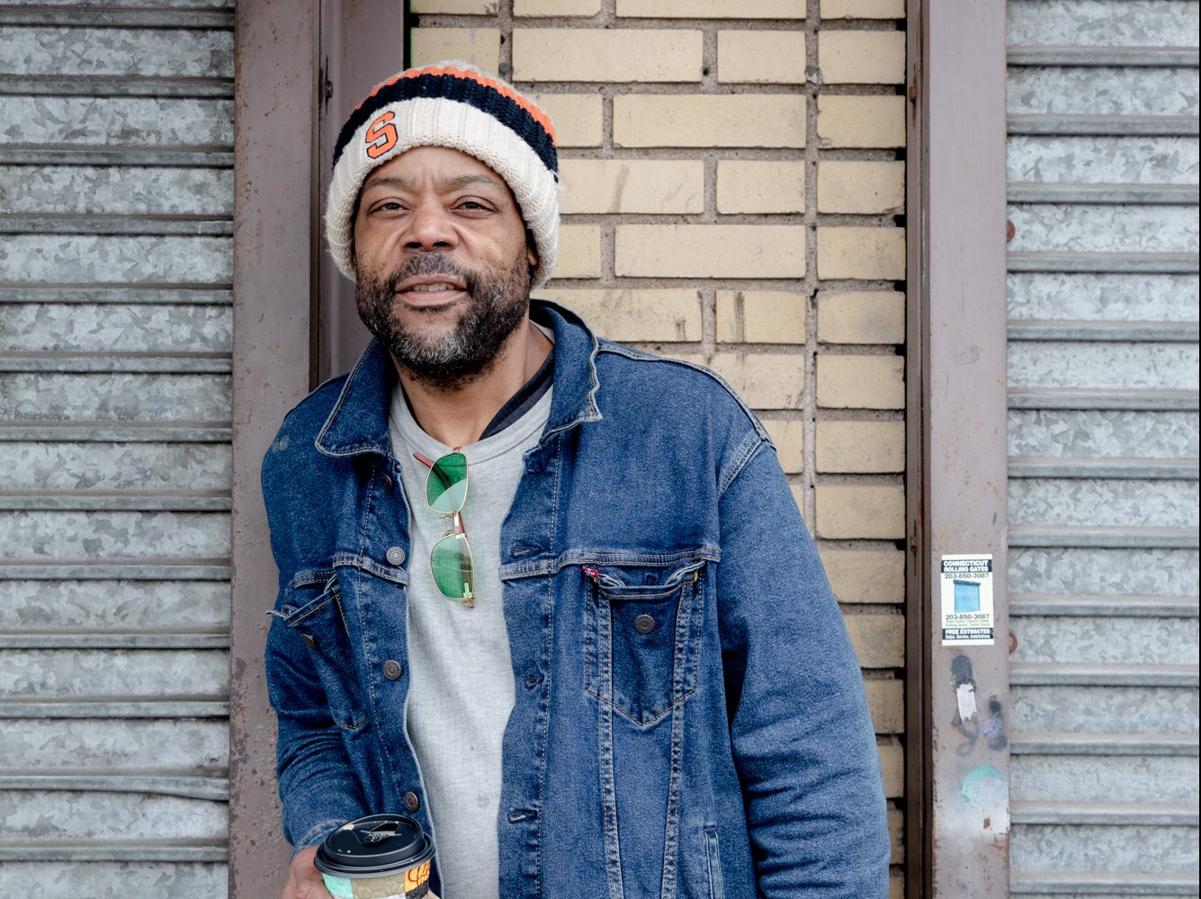 London Jones, a Black man in Hartford, smiles for a photo in front of a building while holding a cup of coffee.