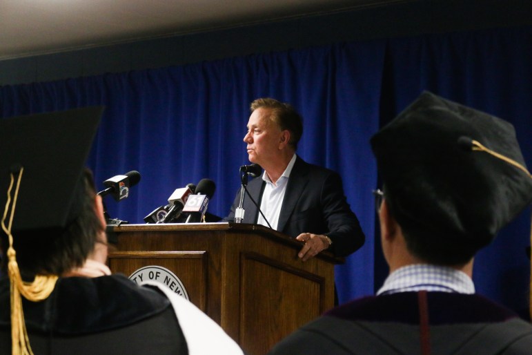 Connecticut Gov. Ned Lamont stands behind a podium, speaking to seven people who've been incarcerated at MacDougall-Walker Correctional Institution and received their associate degrees.