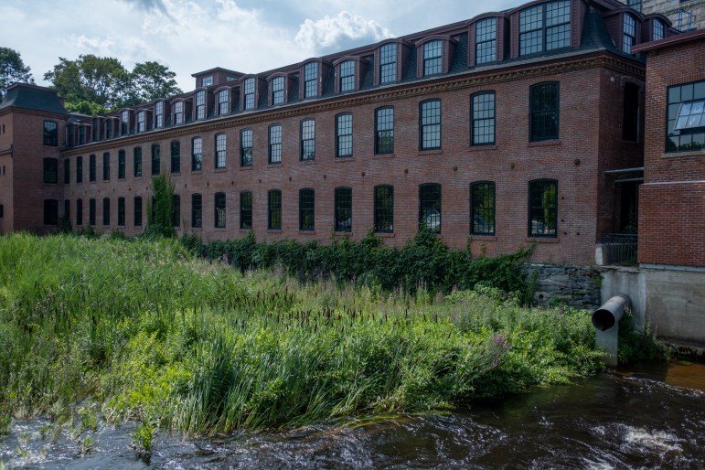 An old mill transformed into an apartment building sits near a patch of grass.