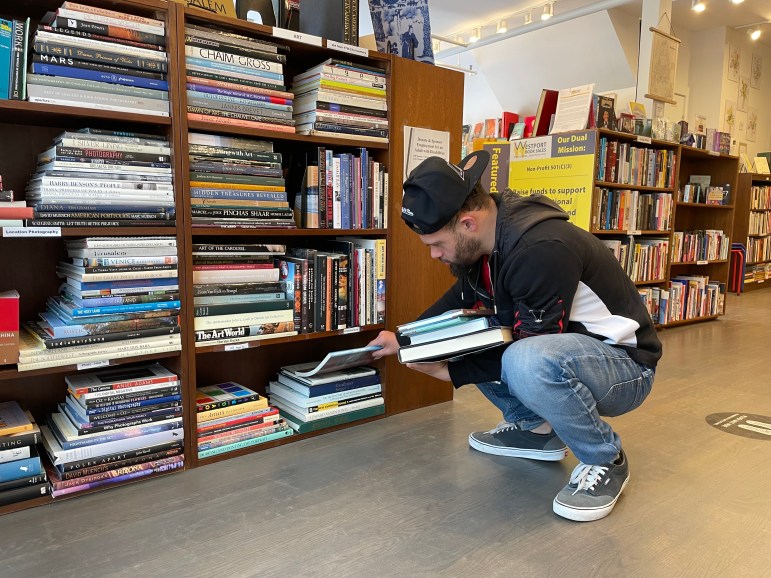 A young man arranges a stack of books on a shelf.