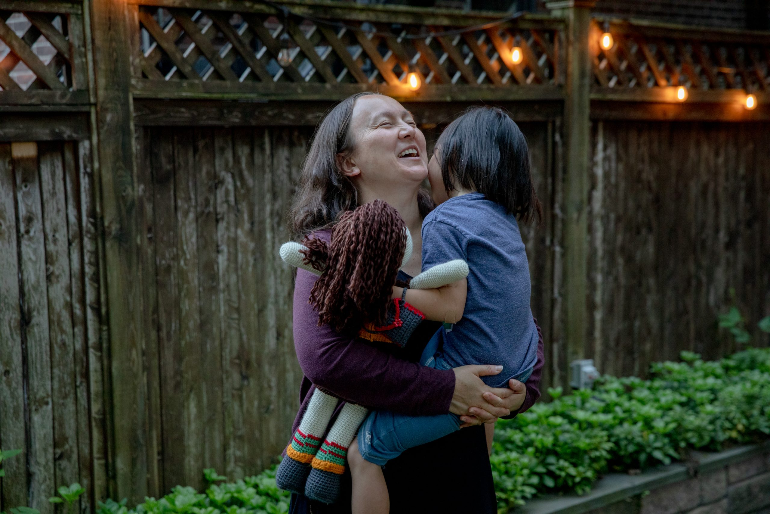 Jennifer stands holding their child, Gabriela. Jennifer is smiling. Their child is holding a rag doll.