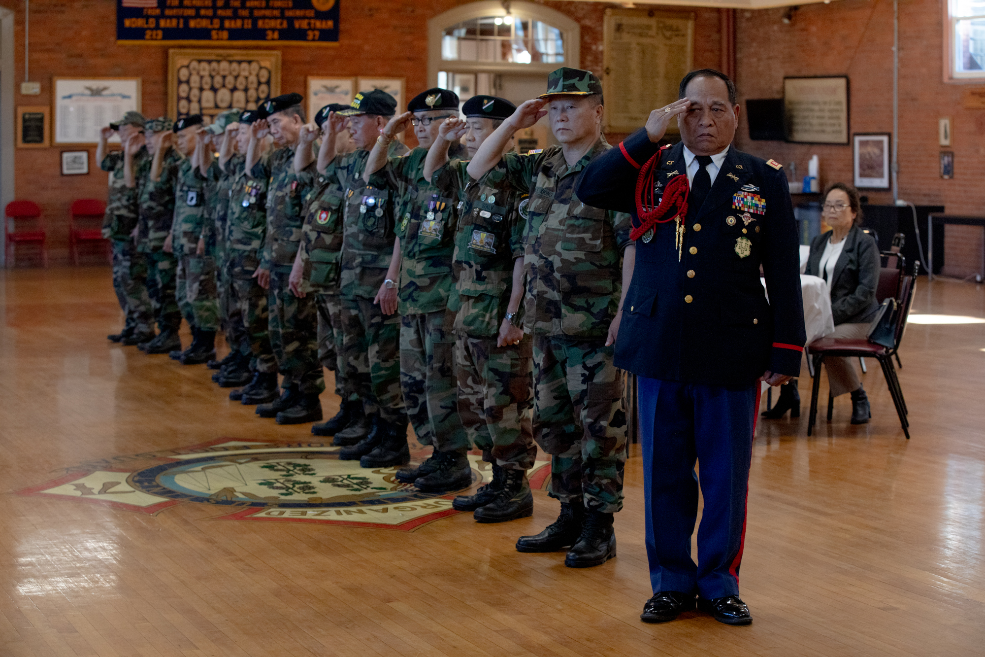 A row of ten men stand in military uniform while saluting.