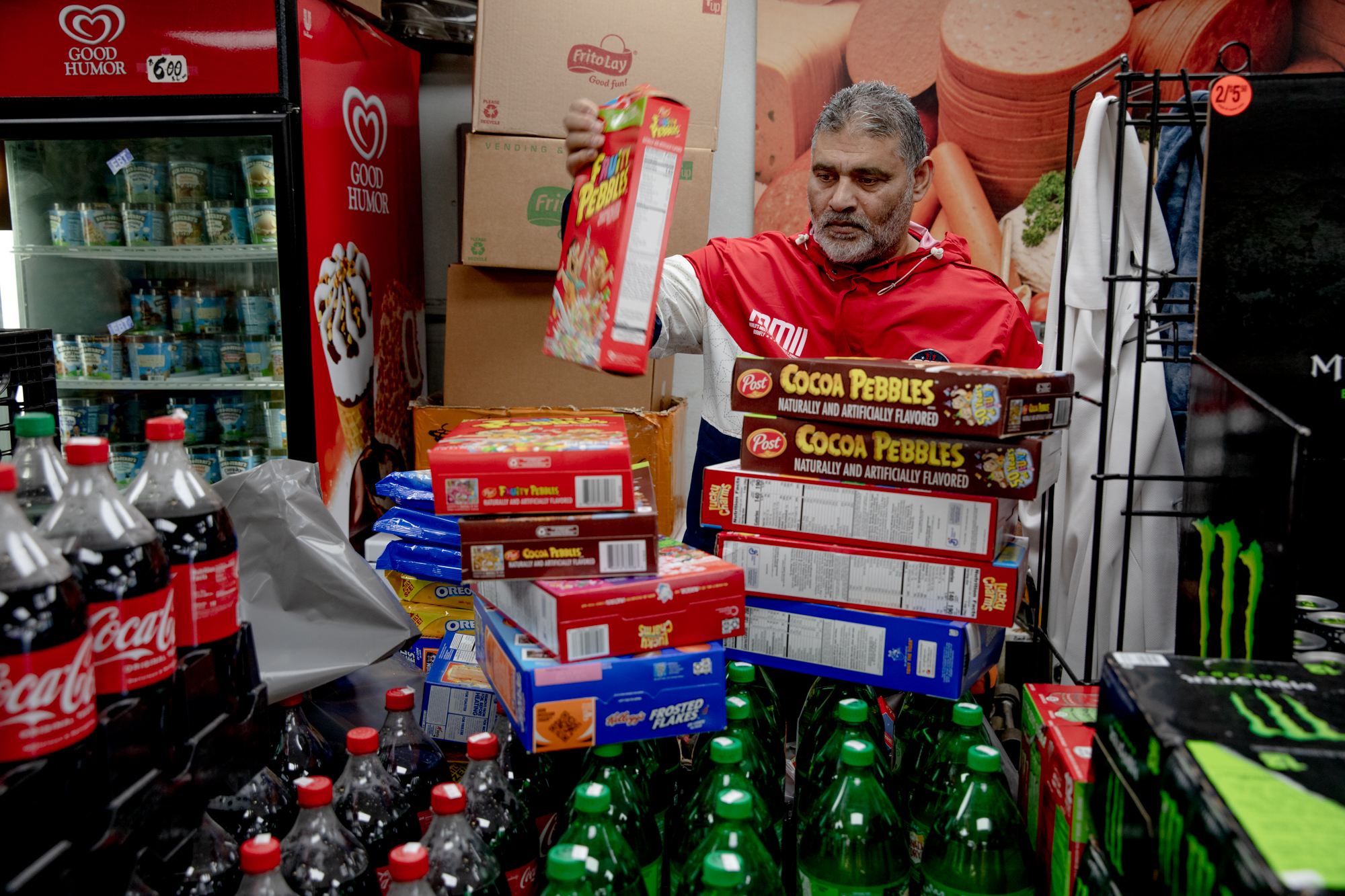 Kamran Kami stands with boxes of cereal stacked on top of crates of soda bottles.